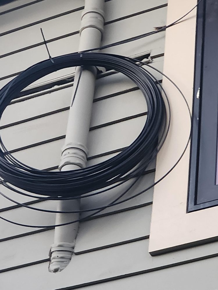 Coiled fiber optic cable run along the side of a house, ready for connection